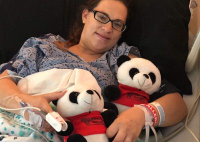 A happy woman celebrates her surrogacy journey with Babytree Surrogacy, holding panda bears in a hospital bed.